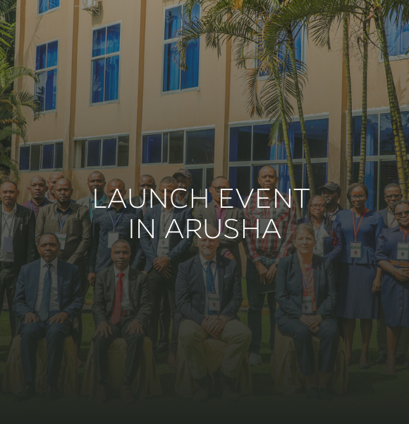 Group photo at a launch event in Arusha, Tanzania in front of a beige building with windows.